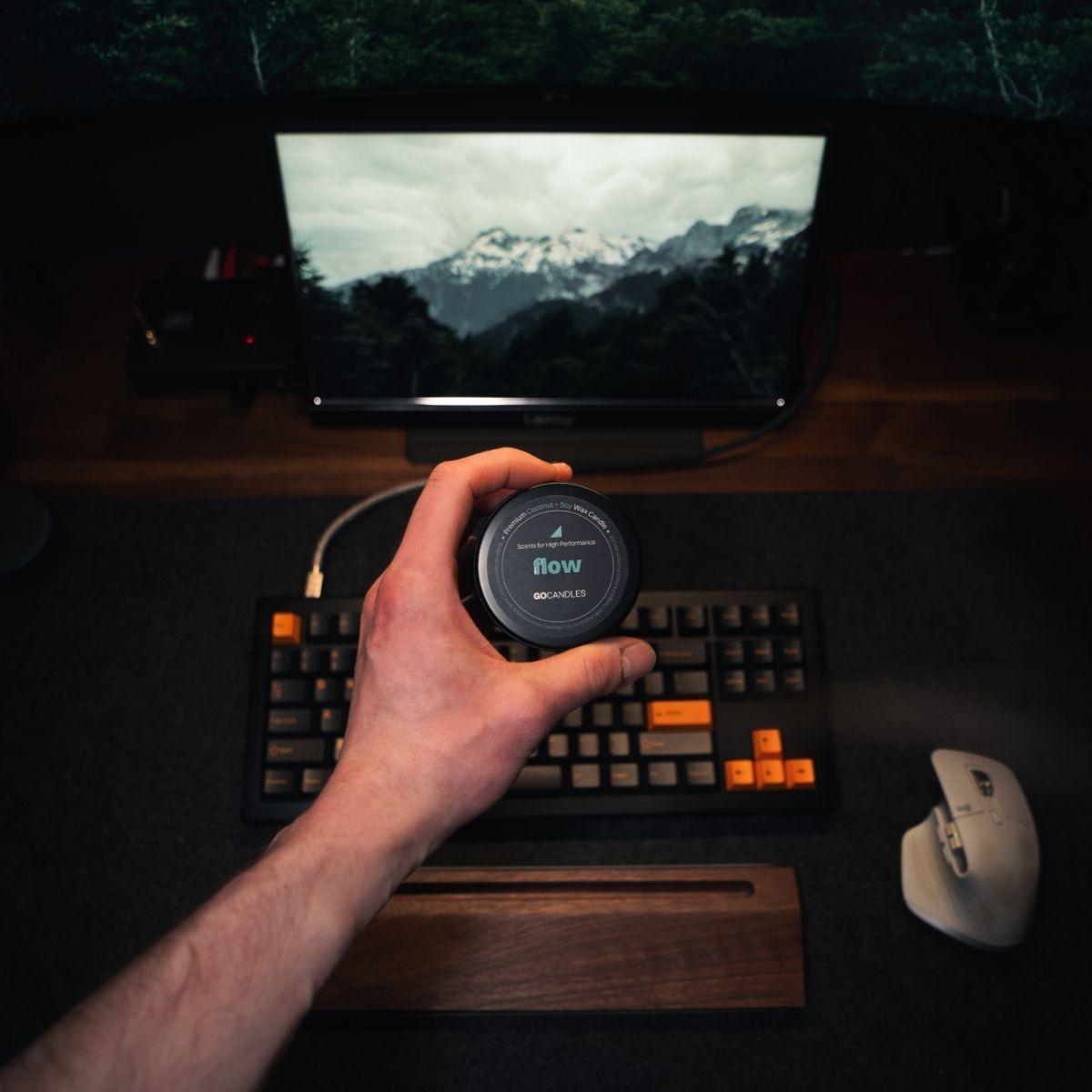 Hand holding Go Candles Flow candle on a desk setup with keyboard and monitor